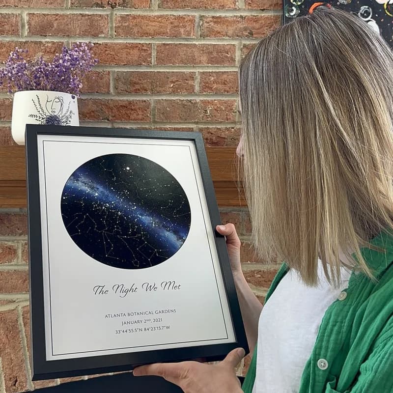 A couple holding a framed star map poster in warm light